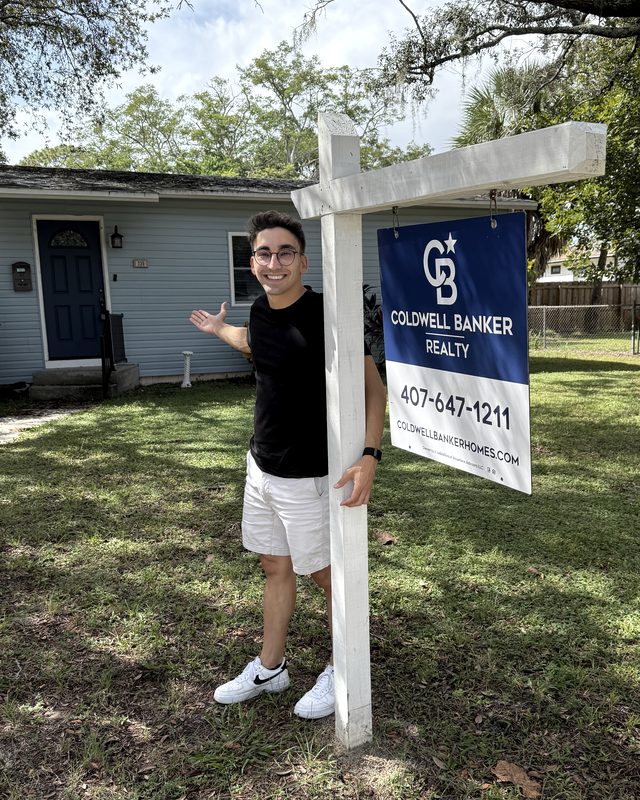 Carlos Galan junto a un cartel de venta de una casa en Estados Unidos